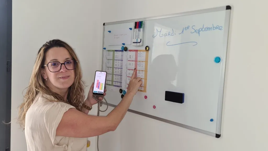 Aurore, assistante maternelle, montre ses plannings du mois imprimés en couleur affichés à son entrée