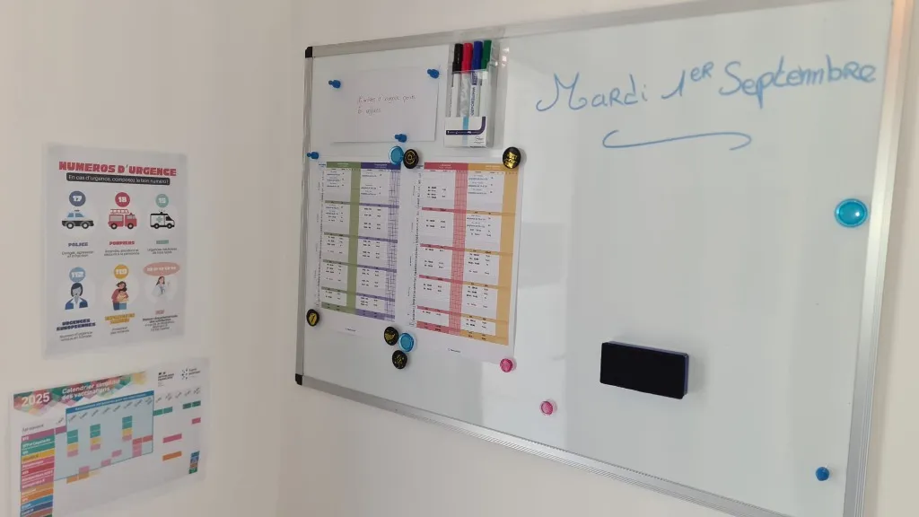 Plannings du mois imprimés punaisés sur le tableau blanc de l'entrée du lieu d'accueil d'Aurore